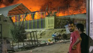 Migrants watch a large fire as it burns inside the Moria refugee camp on the northeastern Greek island of Lesbos, late Monday, Sept. 19. 2016. Greek police say a large fire has swept through a big camp for refugees and other migrants on the eastern Aegean island of Lesbos, forcing its evacuation. None of the more than 4,000 people in the Moria camp was reported injured in Monday's blaze, which damaged tents and prefabricated housing units. (AP Photo/Michael Schwarz)